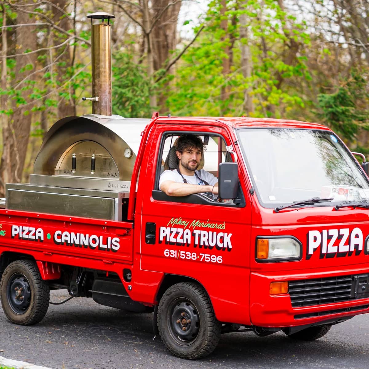 The red pizza truck on the road with its oven in the bed