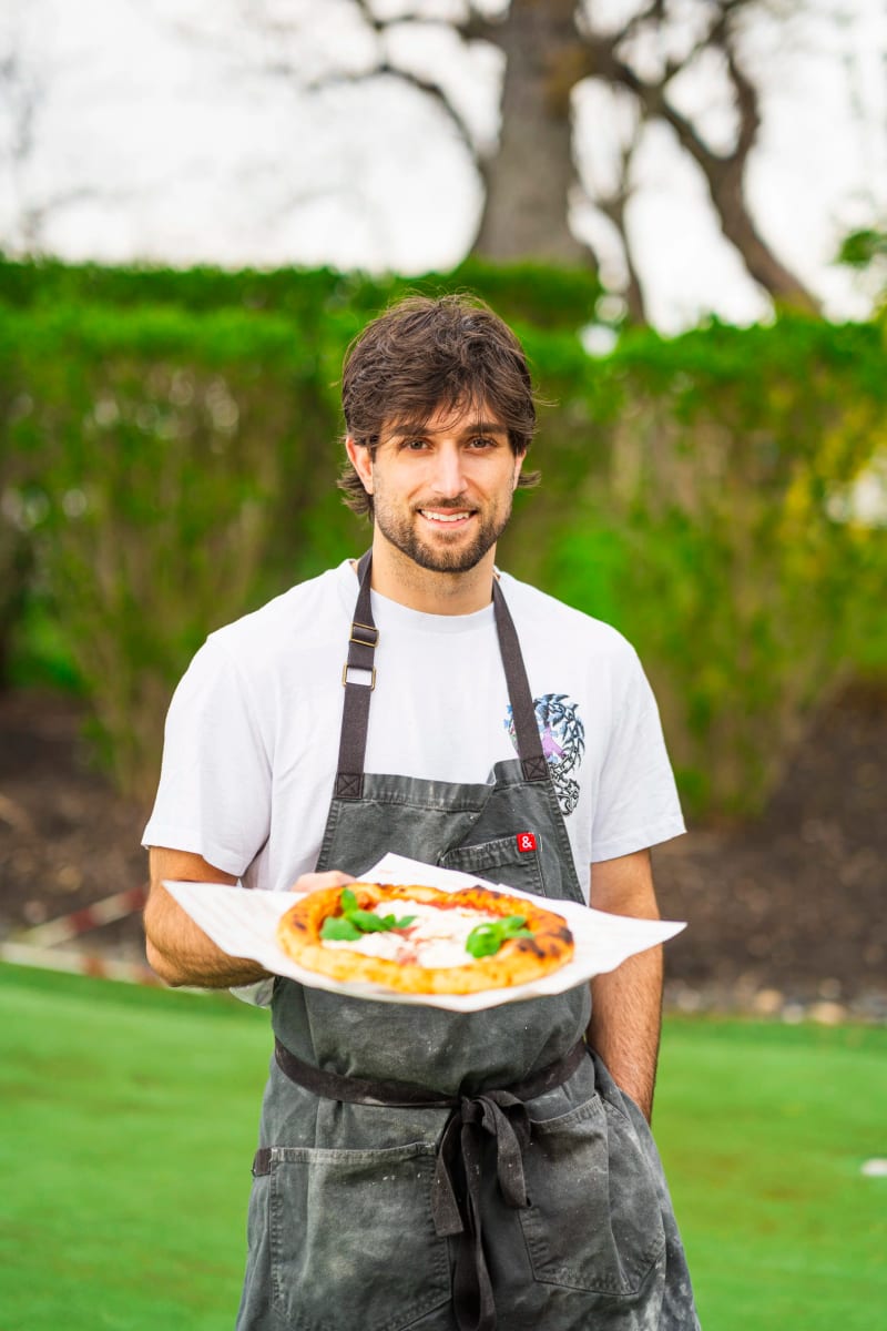 Mikey holding a finished pizza on a lawn