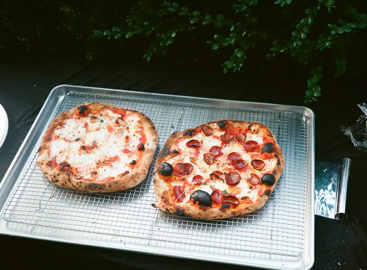Two finished pizzas cooling on a wire rack over a sheet pan